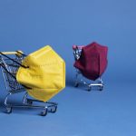 Two miniature shopping carts holding protective face masks on a blue background, symbolizing online product sourcing and B2B marketplace purchasing decisions.