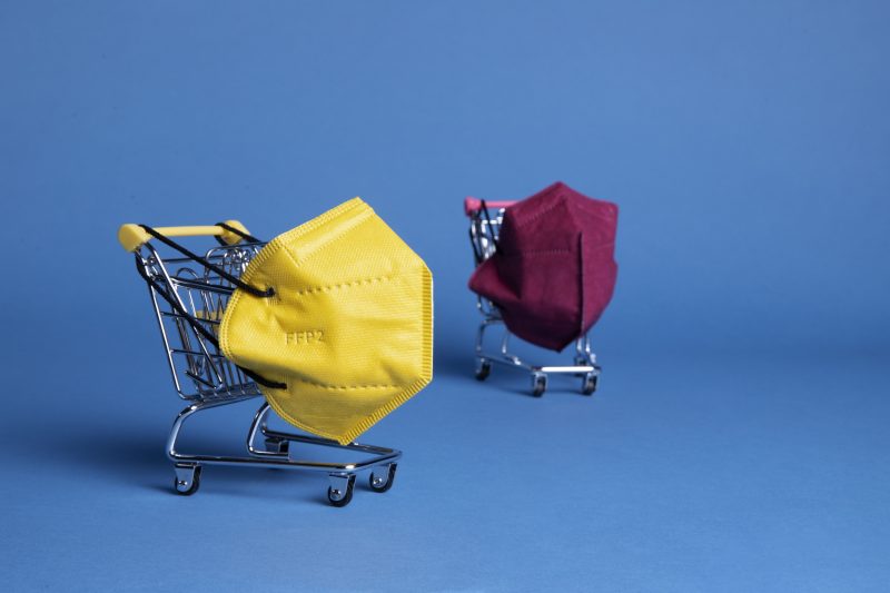 Two miniature shopping carts holding protective face masks on a blue background, symbolizing online product sourcing and B2B marketplace purchasing decisions.